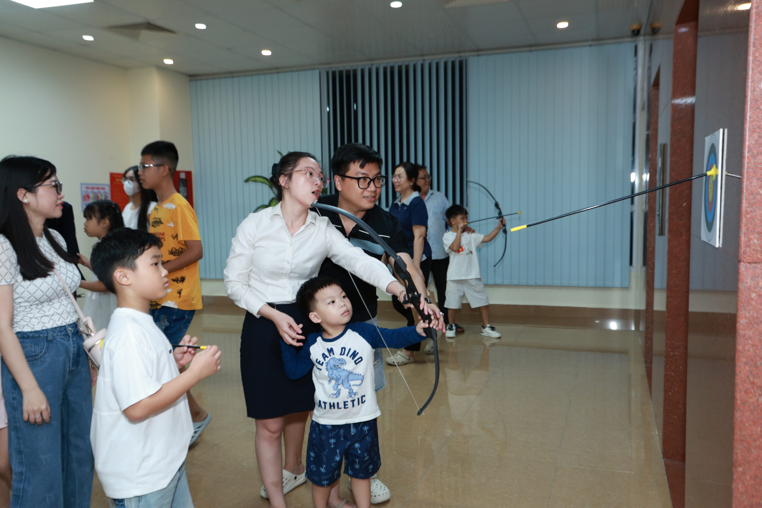 Bố mẹ hướng dẫn con trai nhỏ giương cung bắn tên trúng hồng tâm bia